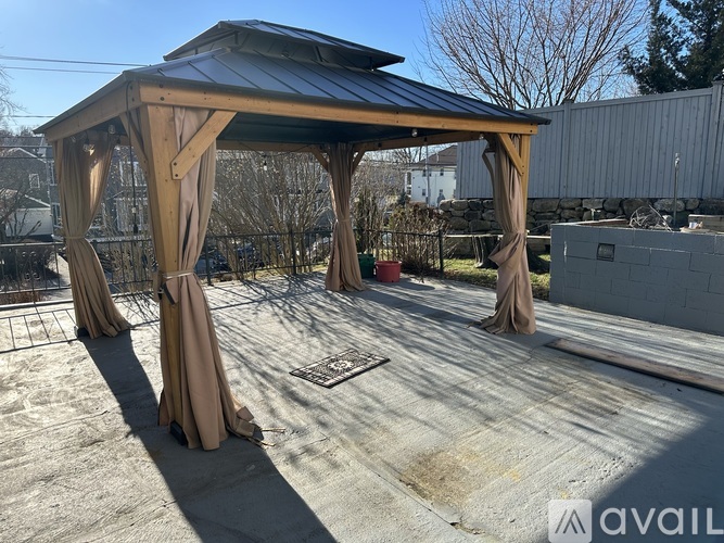 A gazebo with brown drapes is situated on a concrete surface.