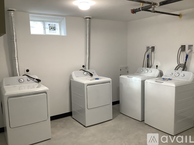 A room with three white washing machines and a window.
