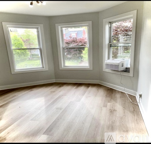 A room with light wood flooring and three windows.