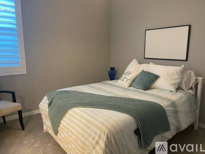A bedroom with a bed covered in a white and beige striped comforter and a blue vase on the bed.