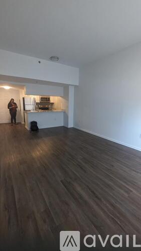 A woman stands in a room with a white wall and wooden floor.