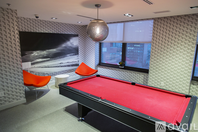 A pool table with a red cloth and a chair in front of a window.