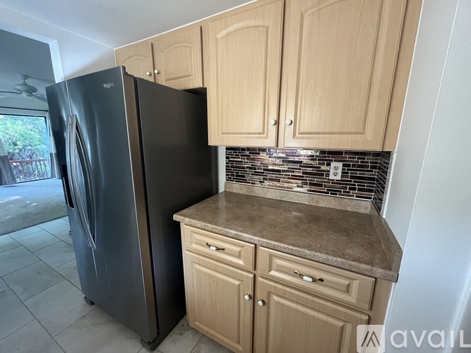 A black refrigerator sits next to a counter with wooden cabinets.