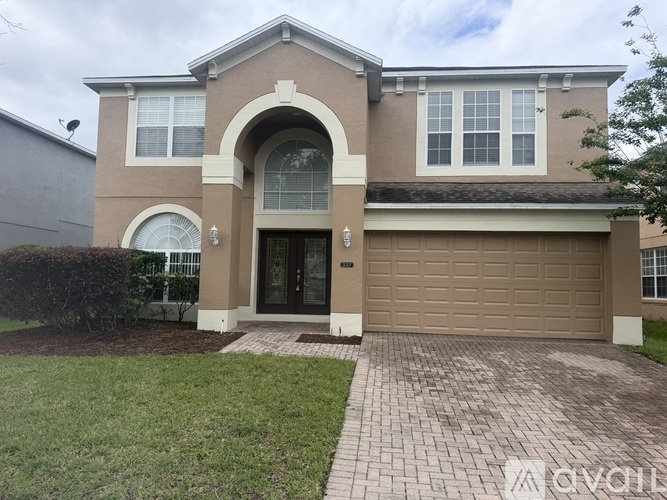 A house with a brown garage door and a brick walkway leading to it.