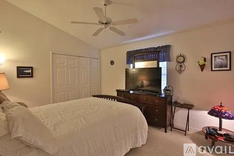 A bedroom with a bed, a television, and a ceiling fan.