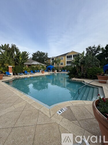 A pool with a blue tiled edge and a stone patio with chairs and umbrellas.
