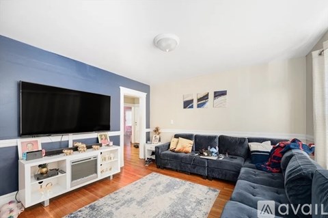A living room with a grey couch and a television on a blue wall.