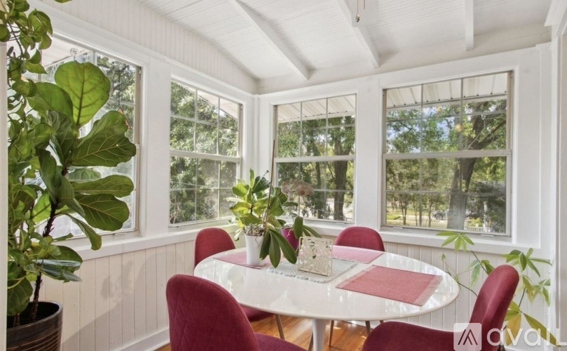 A white table with red chairs is in front of a window with a view of trees.