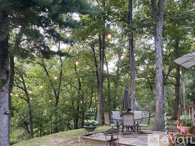 A backyard with a deck and patio furniture surrounded by trees.