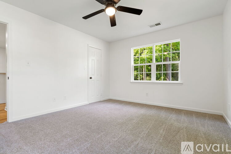 A room with a ceiling fan and a window with a view of trees.