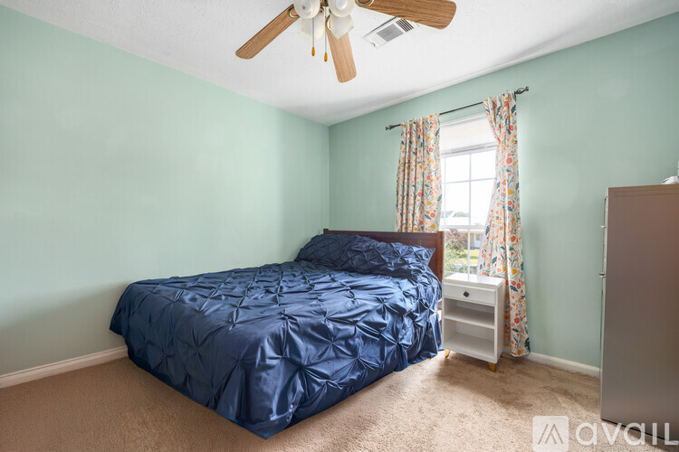 A bedroom with a blue bedspread and a ceiling fan.