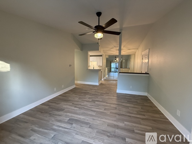 A spacious room with a ceiling fan and light fixture, and a wooden floor.