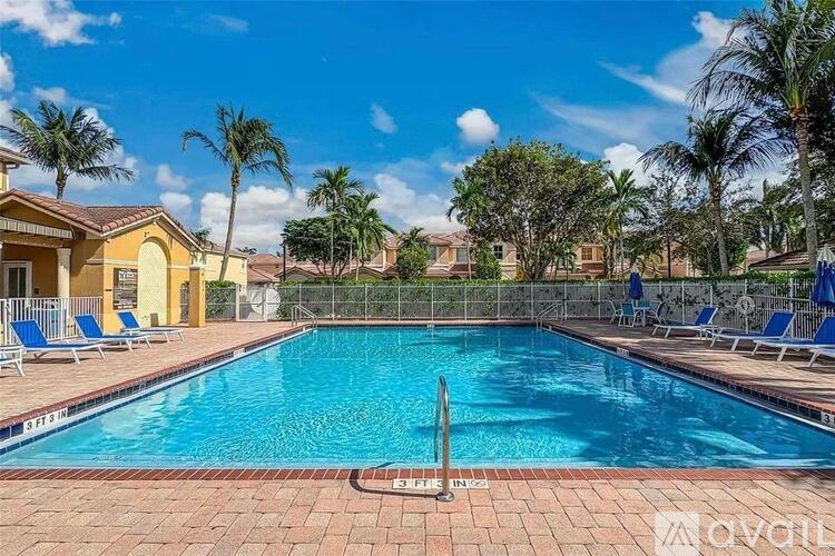 A pool surrounded by blue lounge chairs and palm trees.
