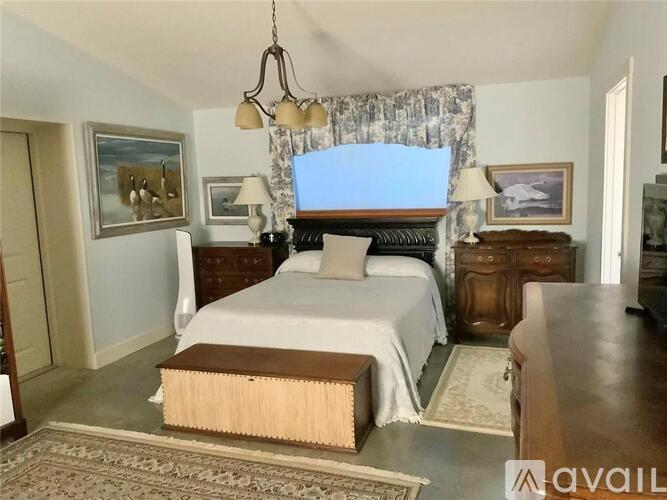 A bedroom with a large bed, a wooden dresser, and a chandelier.
