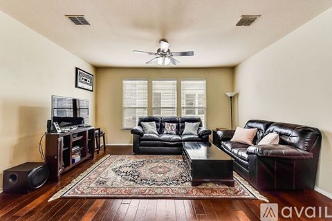 A living room with a black leather couch and a rug.