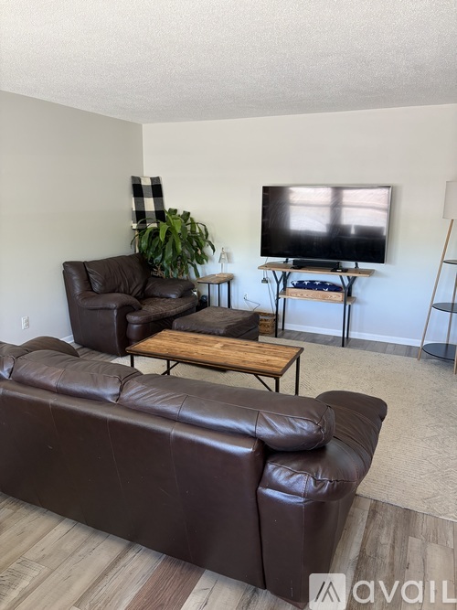 A living room with a brown leather couch, a black and white checkered pillow, a wooden coffee table, and a television on a stand.