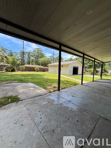 A patio with a concrete floor and a metal railing overlooks a grassy area and a small building.
