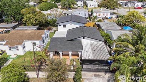 A white house with a black roof is surrounded by greenery.