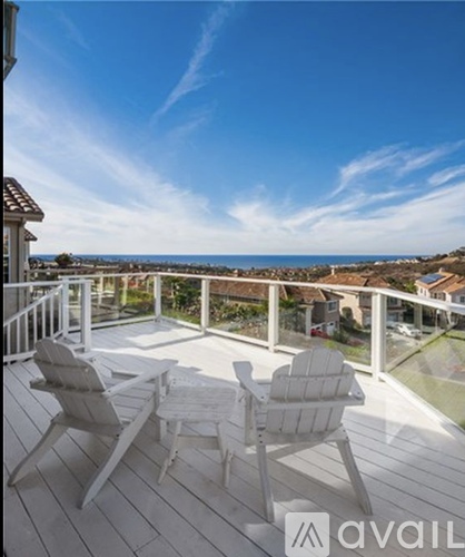 A balcony with two chairs and a table overlooking the ocean.