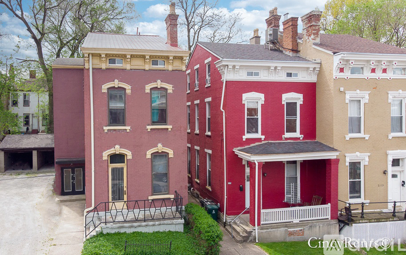 A red building with a white porch and a black fence.
