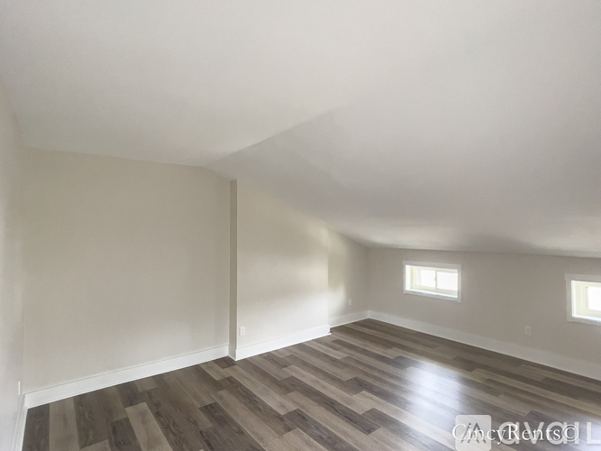 A room with wooden flooring and two windows.