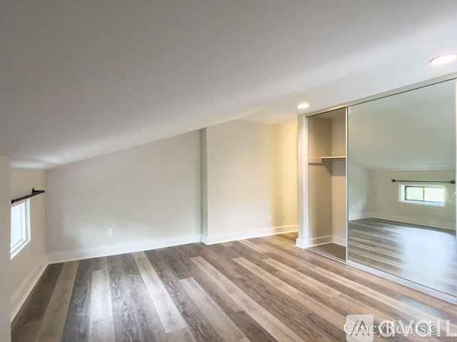 A spacious room with wooden flooring and a large mirror on the wall.