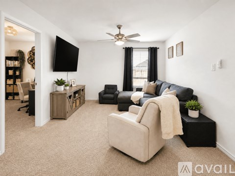 A living room with a beige sofa, a black chair, and a television on the wall.
