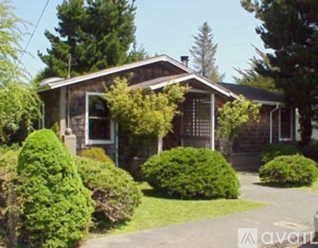 A house with a brown roof and a white door is surrounded by green bushes.