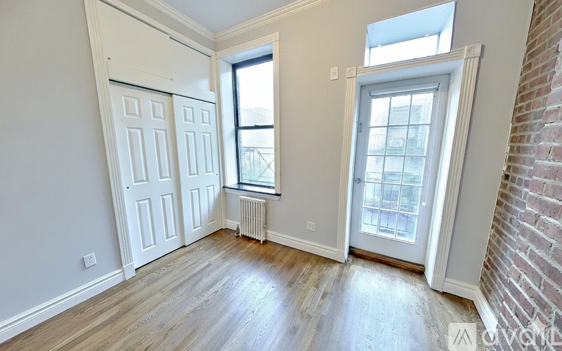 A room with a white door, a window, and a brick wall.