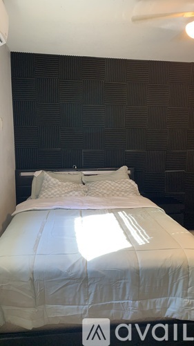 A bed with a white comforter and two pillows sits in a room with a black wall behind it.