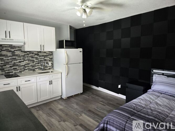 A kitchen with a white refrigerator and a bedroom with a bed and a dresser.