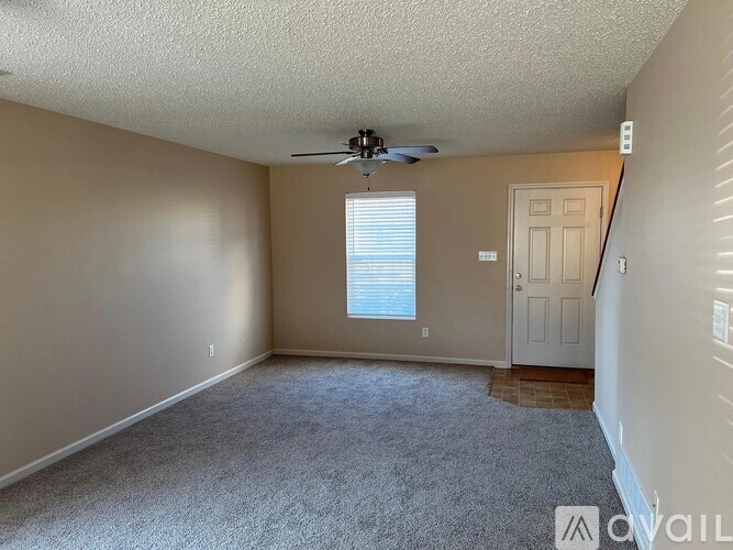 A room with a carpeted floor, a ceiling fan, and a door leading to another room.