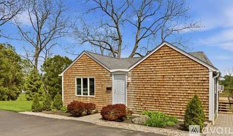 A small wooden house with a grey door and windows surrounded by greenery.