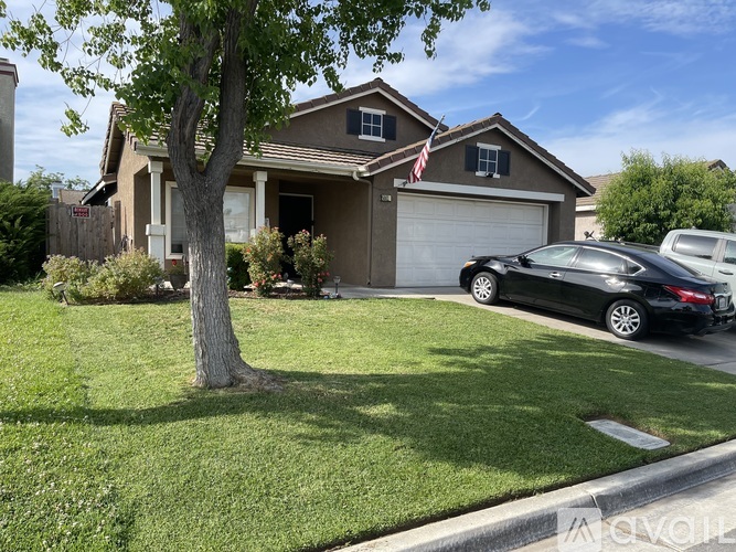 A black car is parked in front of a house with a tree in the front yard.
