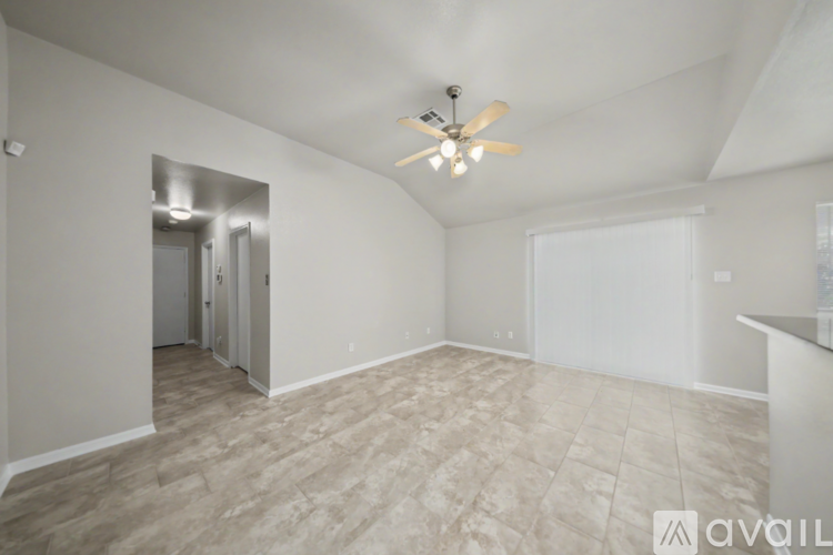 A spacious room with a ceiling fan and light fixture, and a doorway leading to another room.