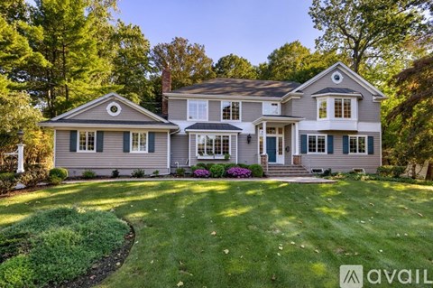 A large house with a well-manicured lawn and trees in the background.