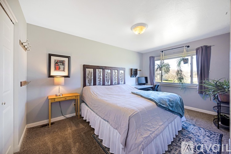 A bedroom with a bed, nightstand, and a window with a view of a plant outside.