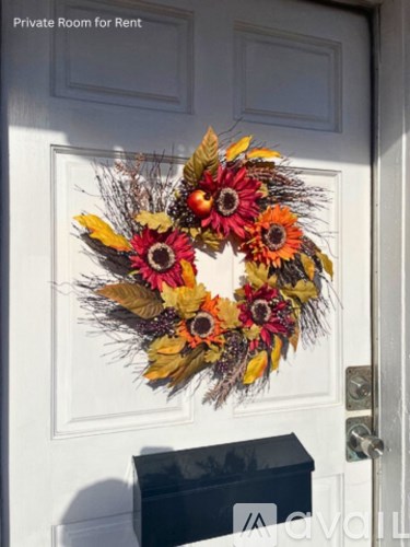 A wreath with flowers and leaves hangs on a white door.