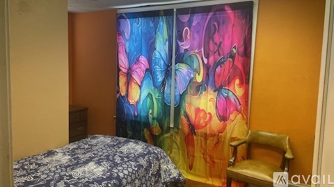 A room with a bed and a chair in front of a colorful curtain.