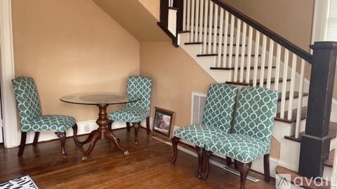 A living room with a round table and two chairs with green patterned cushions.