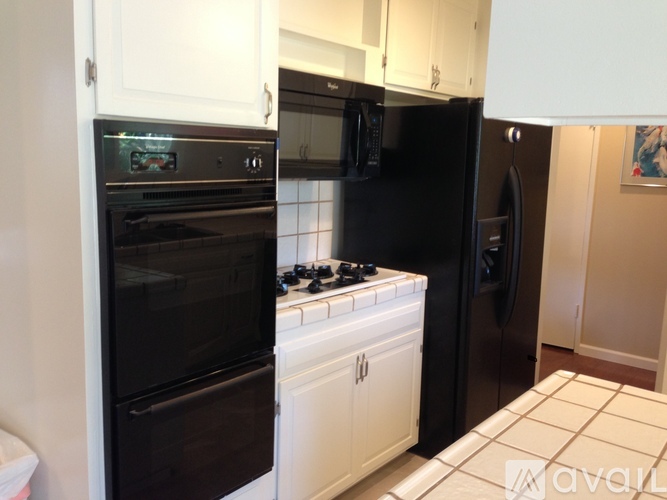 A black fridge and oven in a kitchen with white cabinets.