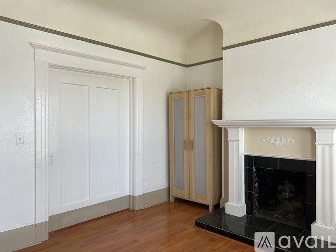 A white fireplace with a black hearth sits in a room with wood floors and white walls.