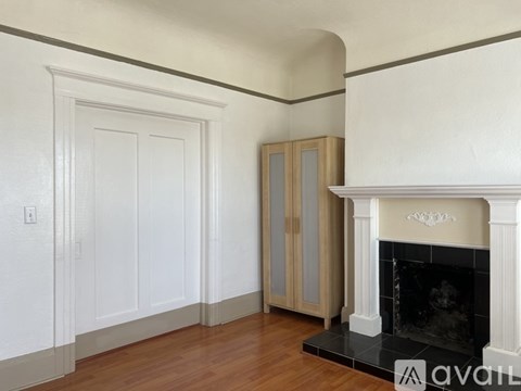 A white fireplace with a black hearth sits in a room with wood floors and white walls.