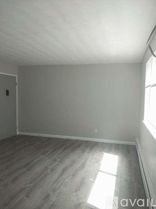 A room with wooden flooring and a window letting in sunlight.