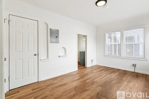 A room with a white door, a window with blinds, and a wooden floor.