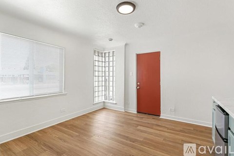 A room with a wooden floor, a red door, and a window with blinds.