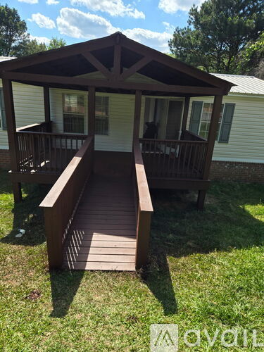 A wooden gazebo with a deck is situated in a grassy area.