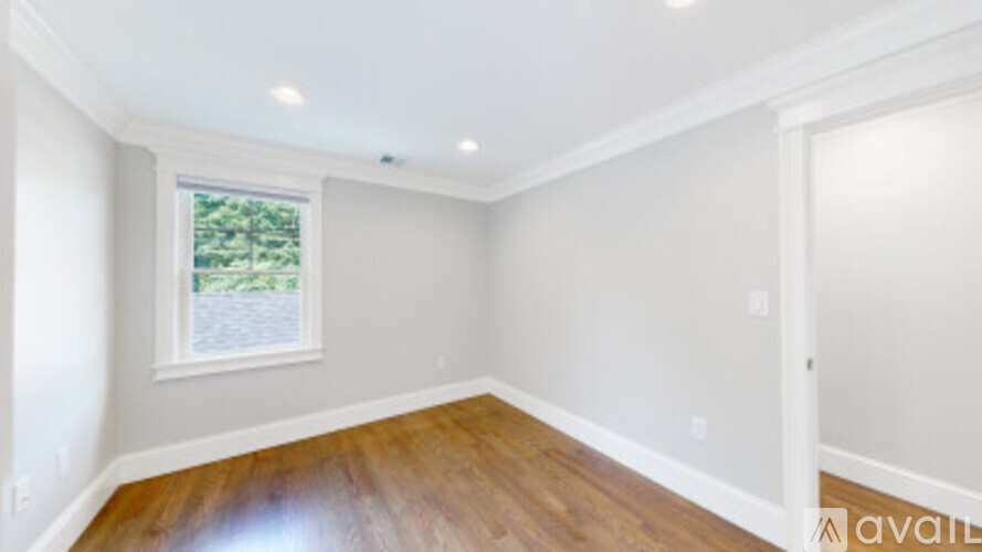 A room with wooden floors and a window showing trees outside.