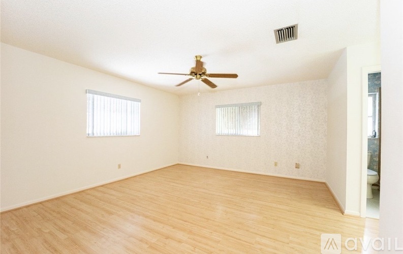 A room with a ceiling fan and two windows.