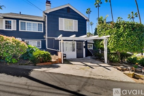 A blue house with a white door and windows is surrounded by greenery.